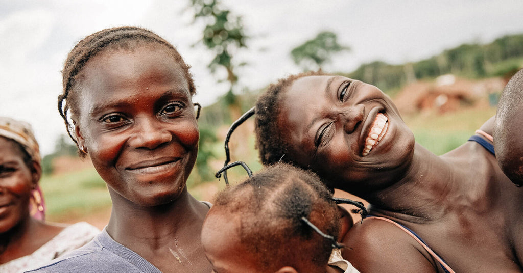 Two african women smile at the camera, one is holding a child