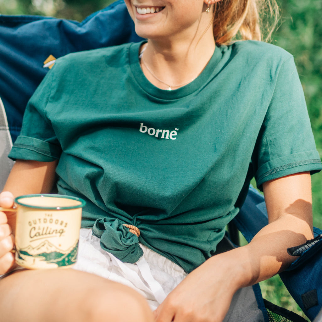 Girl sits on camp chair with mug while wearing a safe and effective mosquito repellent t shirt that repels mosquitos